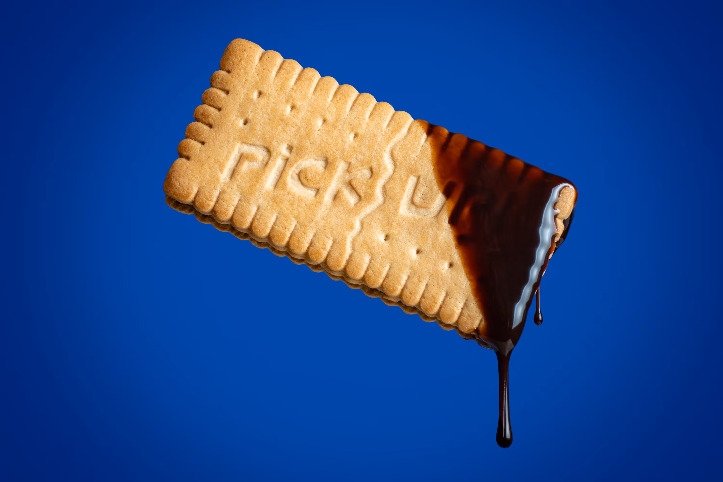 Pick Up biscuit half-dipped in glossy chocolate with drips against blue backdrop, food photography by Photos by Lars.