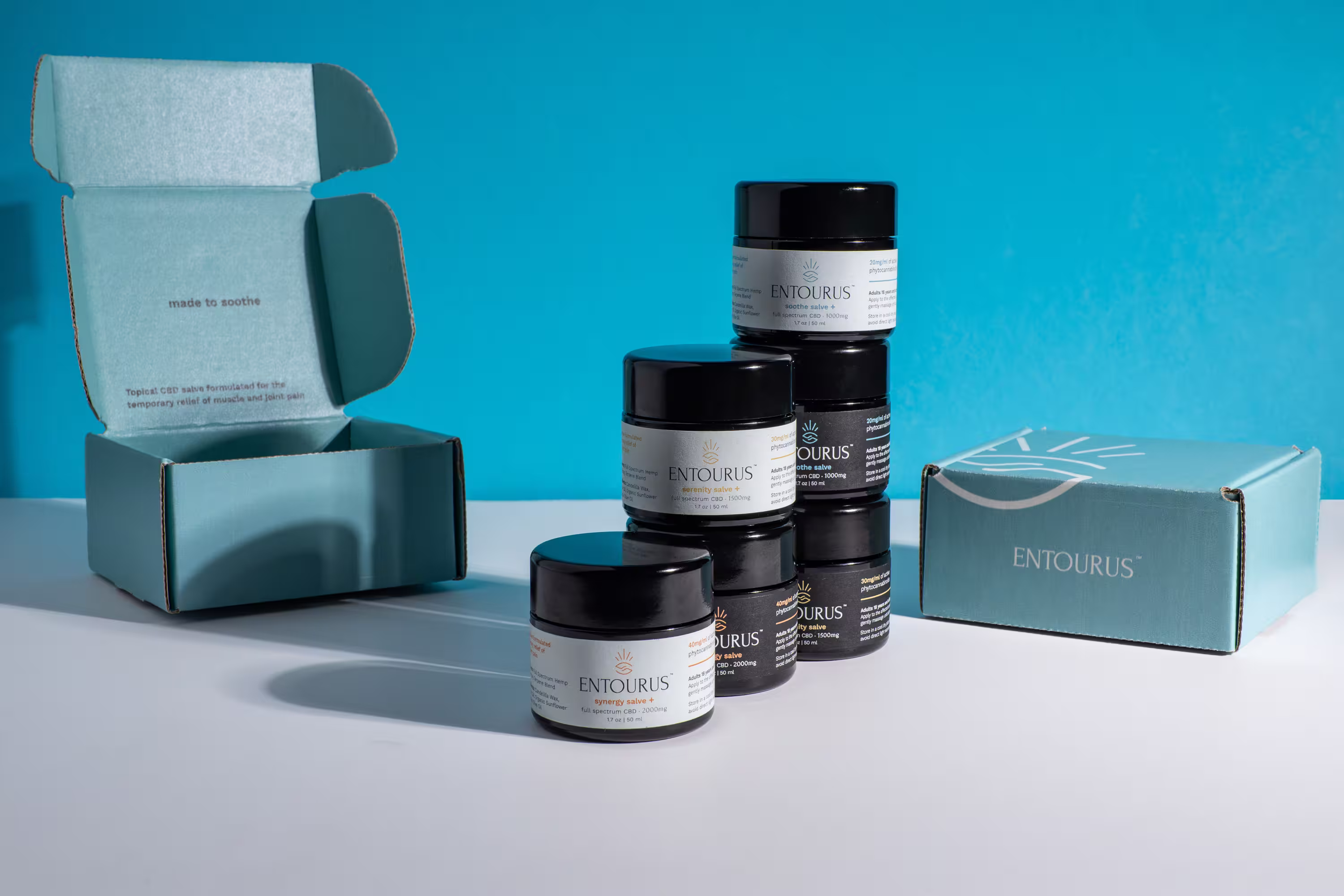 Entourus CBD salve jars with teal shipping boxes on blue backdrop, studio product photography, Photos by Lars.