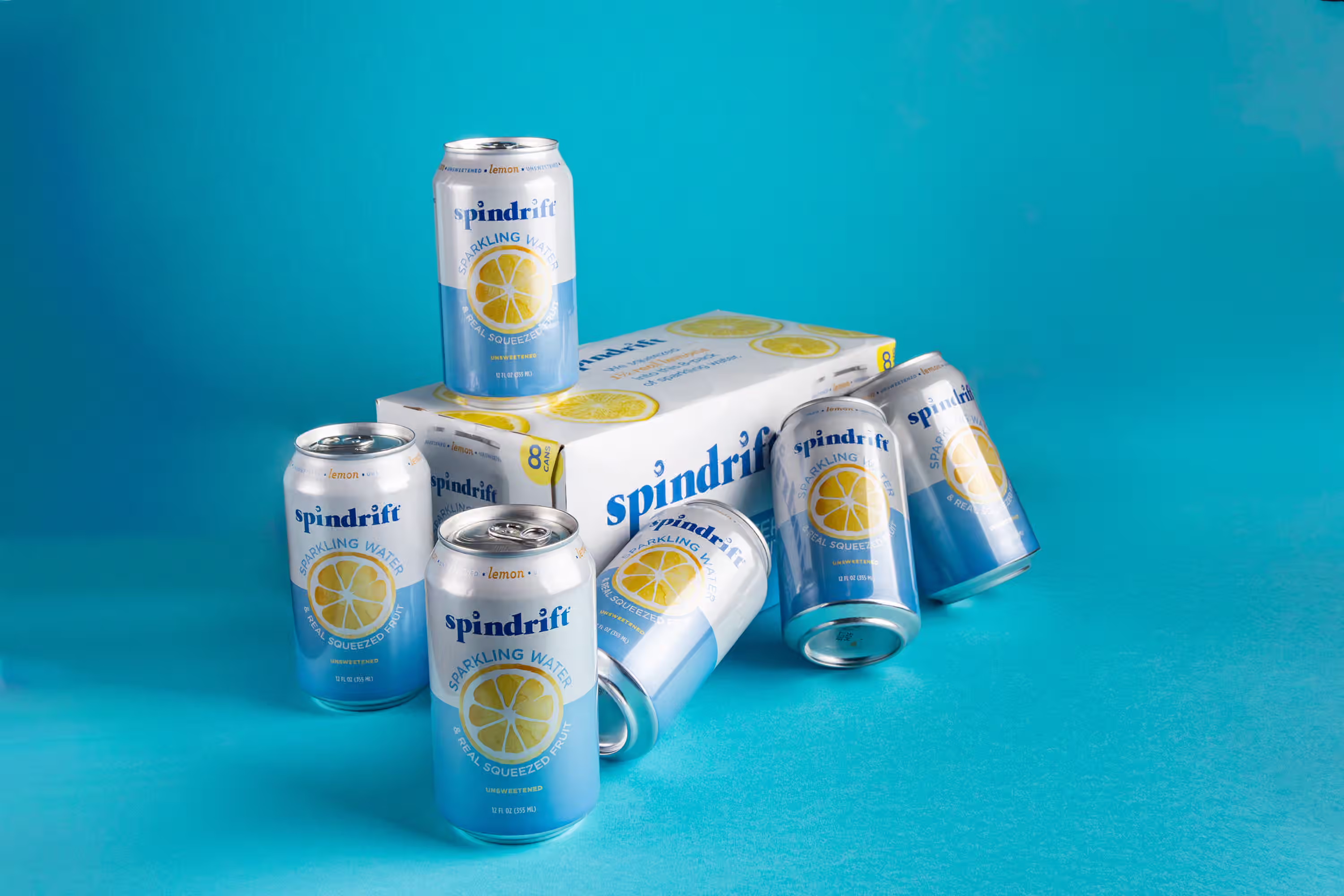 Spindrift lemon sparkling water cans arranged around an 8-pack box on a blue background in a styled product photograph