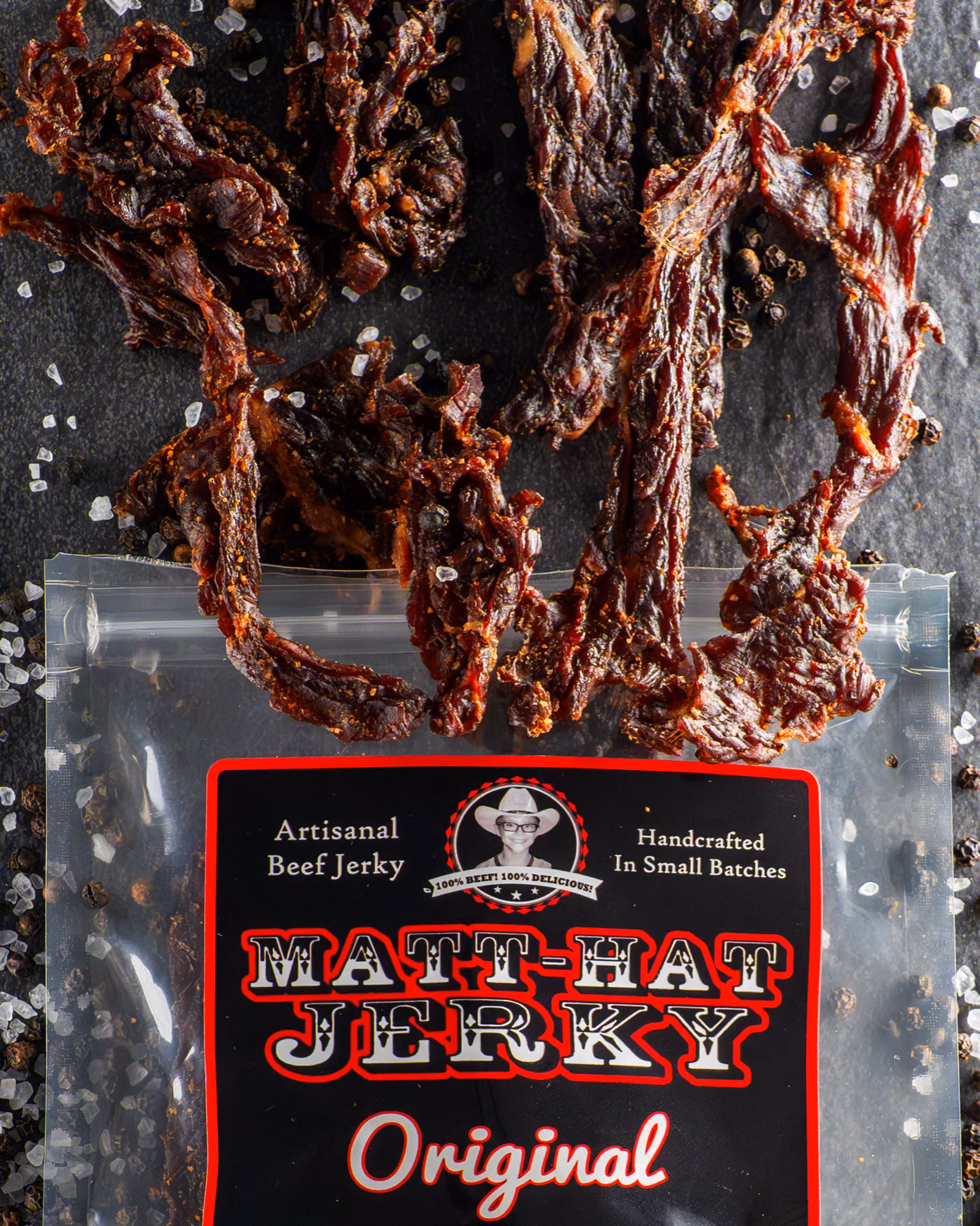 Matt-Hat Jerky Original package with strips of beef jerky and coarse salt on a dark stone background.
